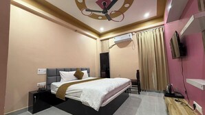 A hotel room with a bed, a ceiling fan, an air conditioning unit, a television, and a wooden desk. - Hotel Anu  (Phulpur)