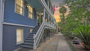 A two-story building with a covered porch, a flag, and a garden with various plants. - Charming Historic Apt Steps to River St & Tours (Savannah)