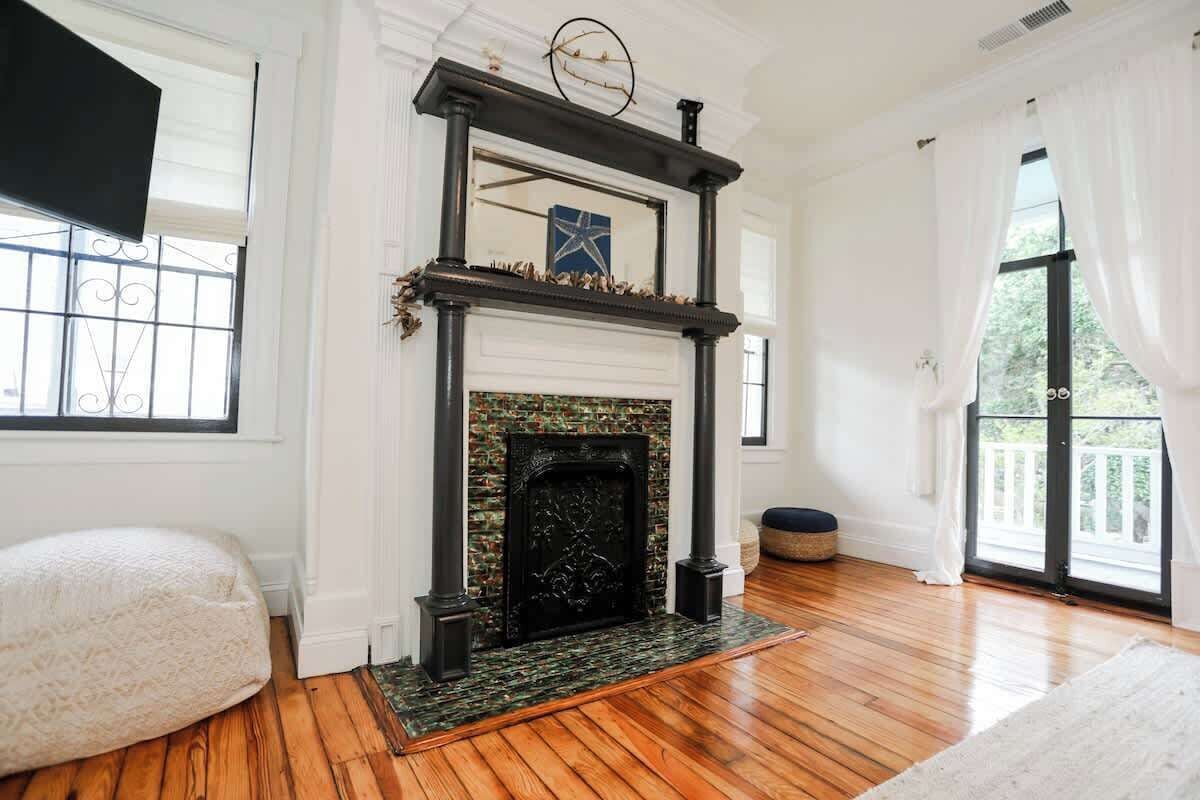 A room with a fireplace, wooden flooring, a white bench, and large windows.