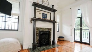 A room with a fireplace, wooden flooring, a white bench, and large windows.