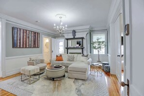 A living room with a sectional sofa, ottomans, a coffee table, a chandelier, a fireplace, and a bookshelf.