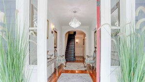 A hallway with a chandelier, a staircase, and a patterned rug.