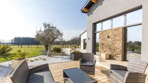 Un patio moderno al aire libre con mobiliario de mimbre, una pared de piedra y vistas a un campo verde.