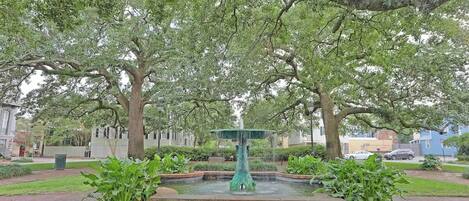 A fountain surrounded by brickwork, with trees and a paved walkway.