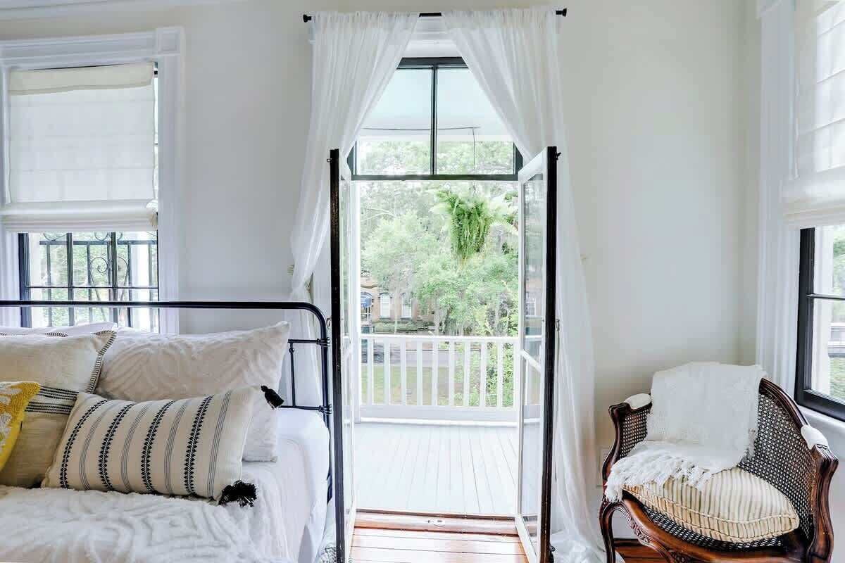 A room with a bed, a chair, and a balcony with a view of greenery.