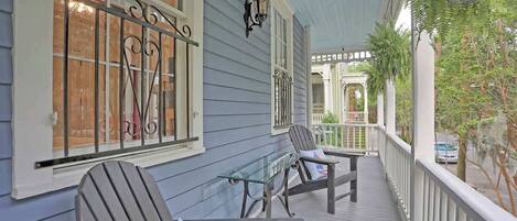 A porch with Adirondack chairs, a glass table, and a white railing.