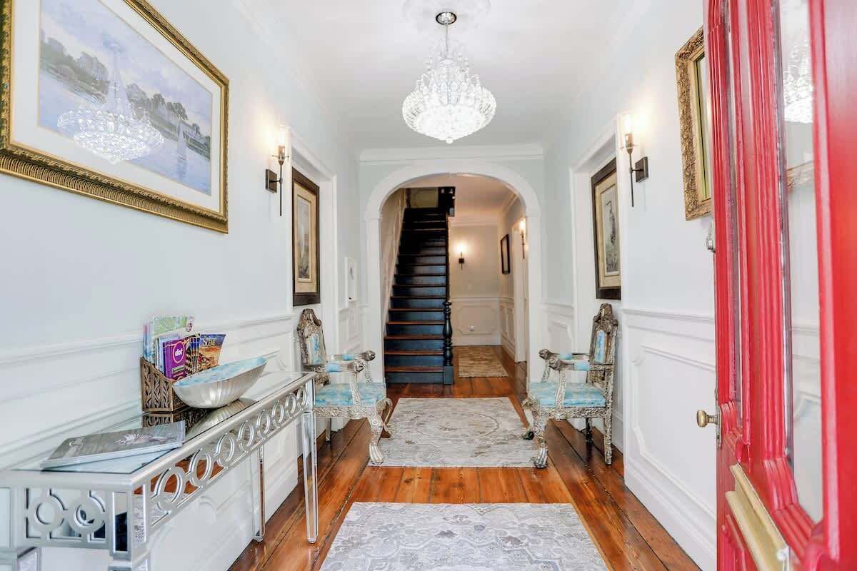 A hallway with a staircase, a chandelier, and a red door.