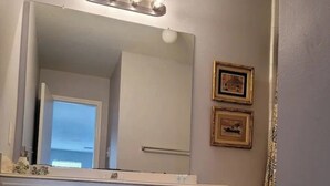 Un baño con tocador blanco, un espejo grande con luces, un inodoro y cuadros en la pared.