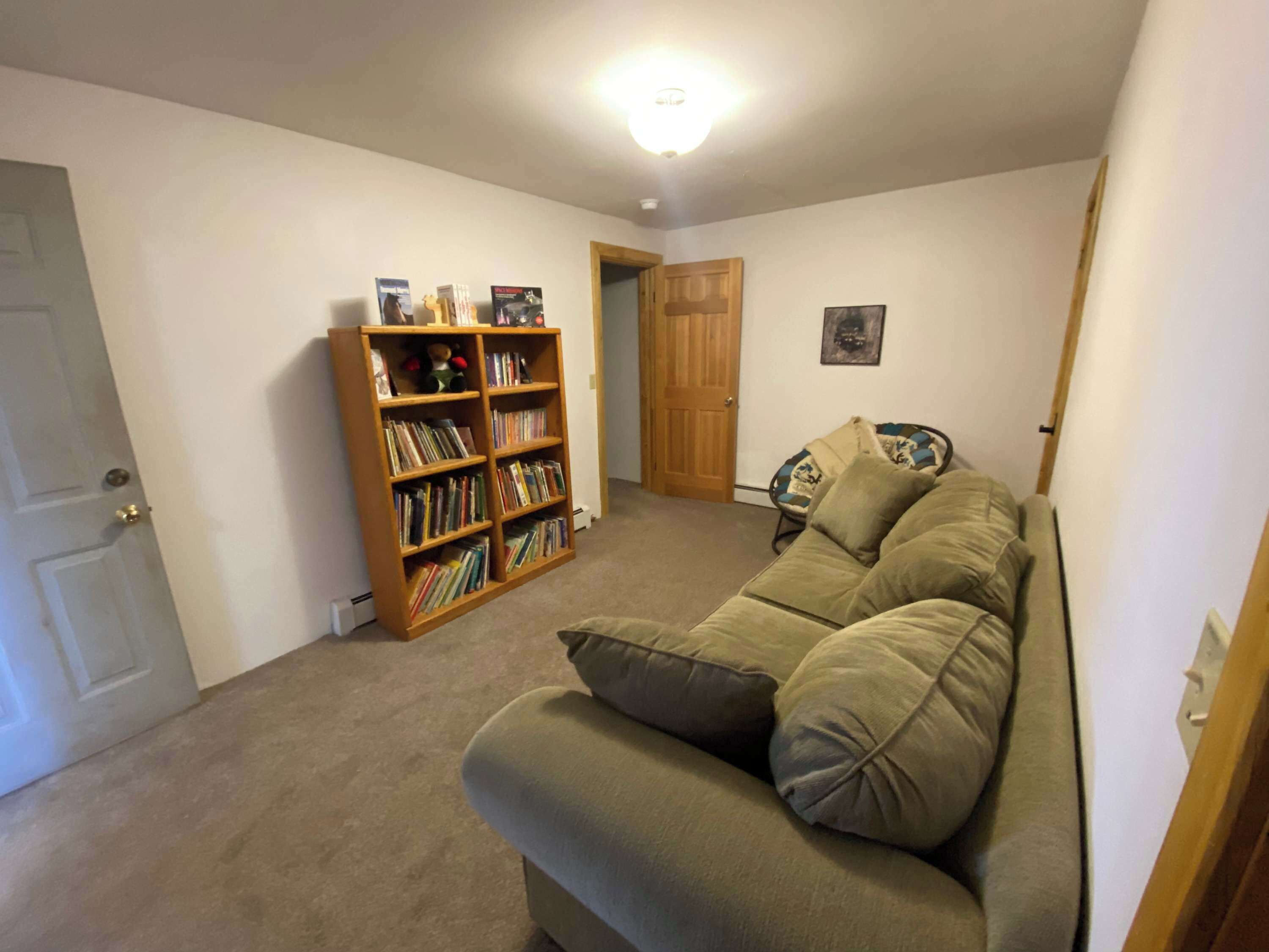 A living room with a beige sofa, a bookshelf, and a door.
