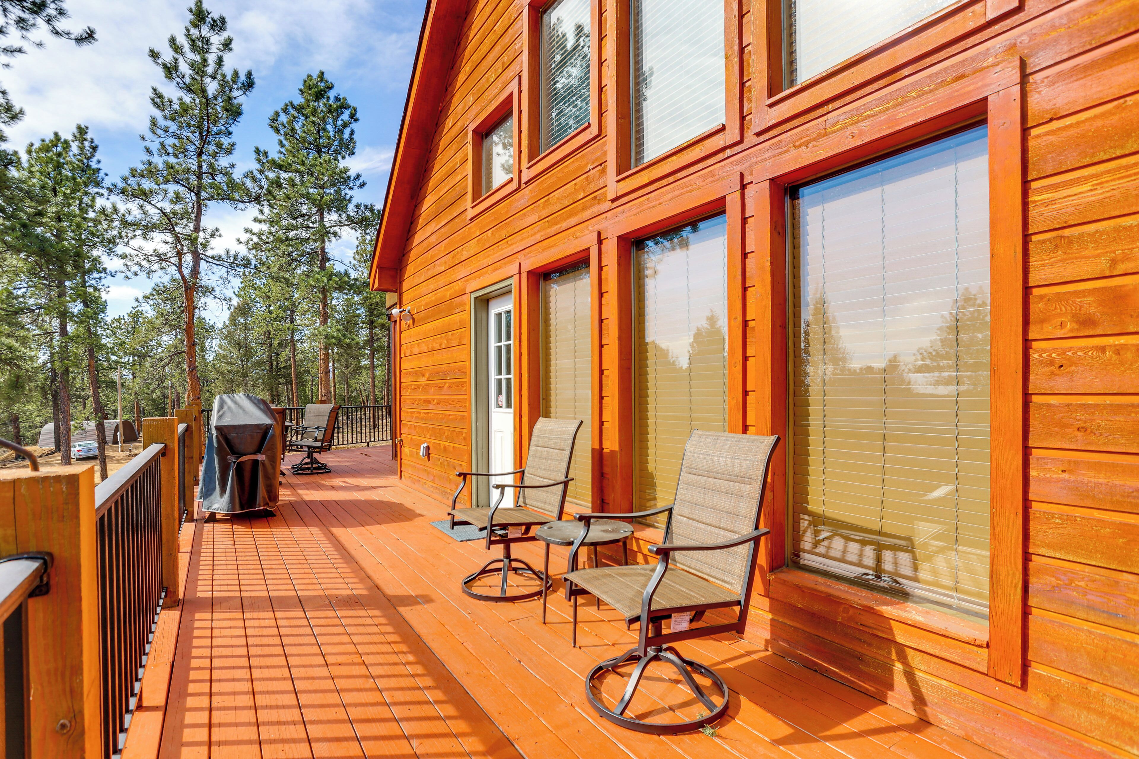 A wooden deck with outdoor furniture, a grill, and a view of a forest.