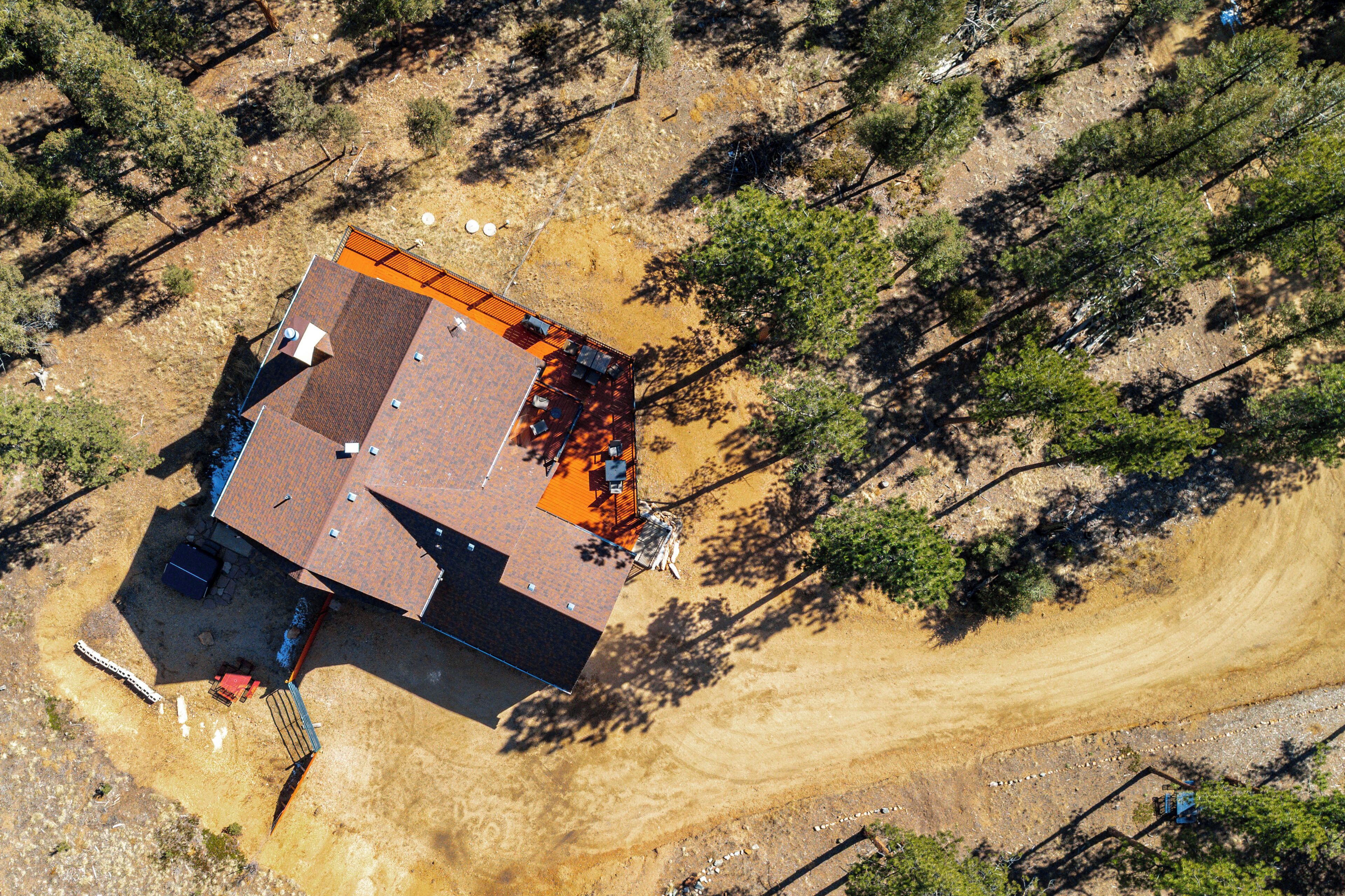 An aerial view of a house with a red roof, surrounded by trees and a dirt path.