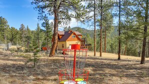 Una casa rodeada de bosque, con un cesto de disc golf al frente.