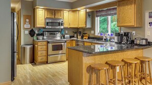 A modern kitchen with wooden cabinets, stainless steel appliances, and a central island with stools. - 2 Mi to Woodbury Wildlife Area: Cozy Farmhouse! (Warsaw)
