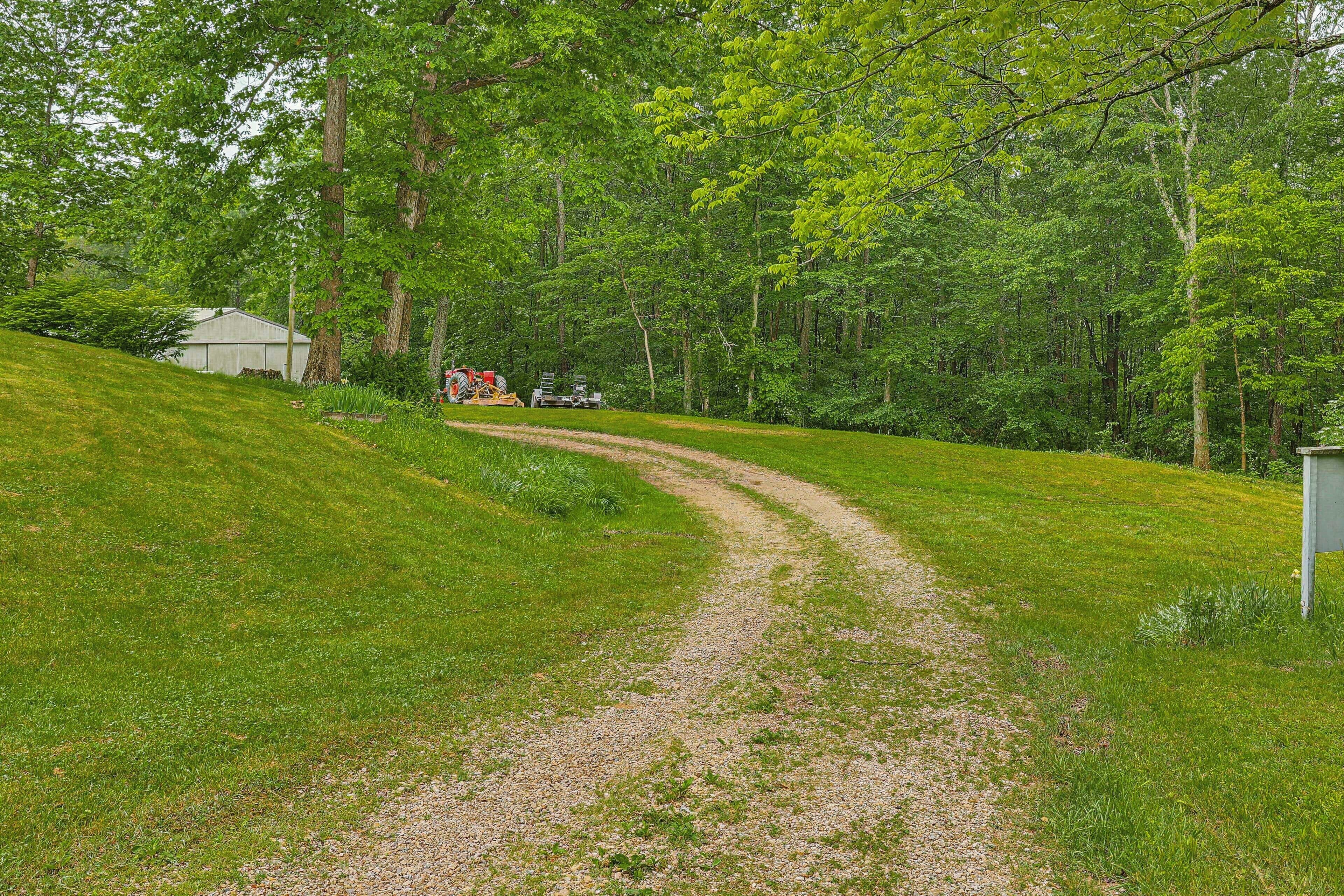 Un chemin de gravier dans une zone boisée, avec un petit bâtiment et un camion au loin.