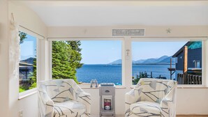 Una habitación con dos sillones estampados orientados hacia un ventanal con vistas a un lago y montañas.