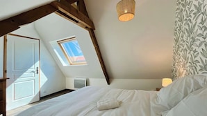 A bedroom with a sloped ceiling, a skylight, a bed with white bedding, a hanging light fixture, and a floral wallpaper pattern.