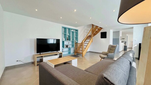 A modern living room with a flat-screen TV, a sofa, a coffee table, a staircase, and a bookshelf.