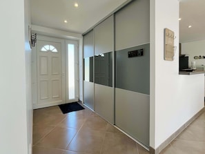A hallway with a sliding door, a black mat at the entrance, and a wall-mounted light fixture. - Gîte de la Fontaine - Family house in Carentan (Carentan-les-Marais)