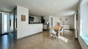 A modern kitchen with a central island, a dining area with a wooden table and chairs, and a large window providing natural light.