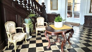 A grand hallway with a checkered floor, ornate chairs, a wooden table with a potted plant, and a staircase with dark balusters. - Elegant Chateau Escape for 2 - Nature & Calm (Nointot)