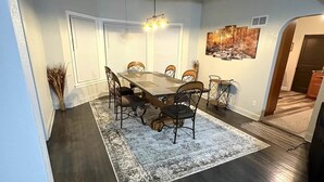 Uma área de refeições com uma mesa e cadeiras de madeira, um tapete e um quadro na parede.