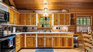 Una cocina tipo cabaña de madera con una isla grande, armarios de madera, horno empotrado y una lámpara colgante.