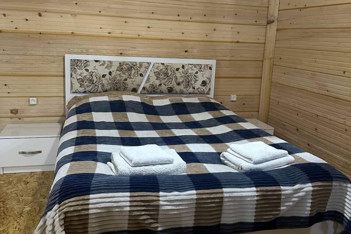 Habitación con paneles de madera, una cama, una mesita de noche y un interruptor de luz en la pared.