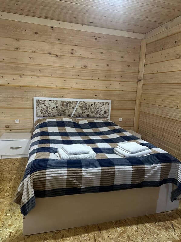 Une pièce aux murs lambrissés, comprenant un lit, une table de chevet et un interrupteur fixé au mur.