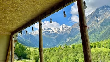 Un balcón de madera con vista a montañas nevadas y vegetación exuberante.