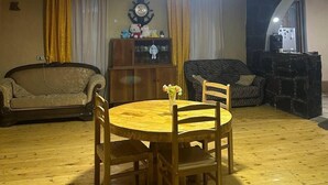 A living room with a round wooden table and four chairs, a sofa, a cabinet with decorative items, and a ceiling light fixture. - Qvis sakhli (Mestia)