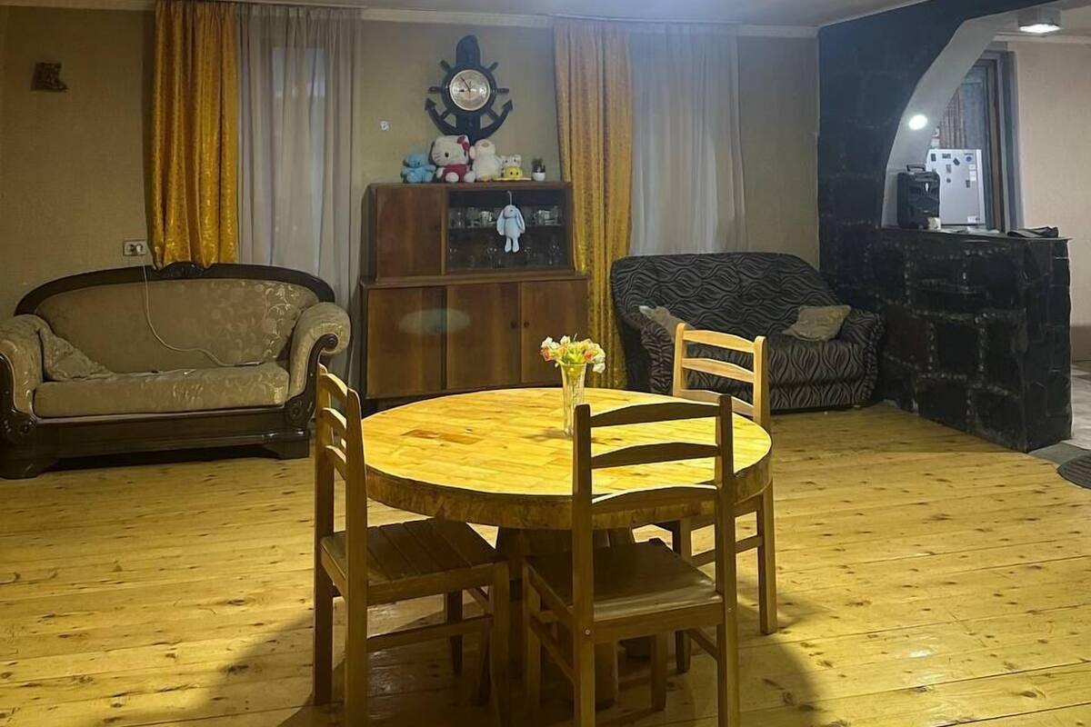 Una sala de estar con una mesa redonda de madera y cuatro sillas, un sofá, un aparador con adornos y una lámpara en el techo.