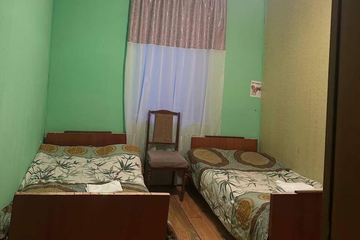 Una habitación con dos camas de madera, una silla, una lámpara en el techo y una ventana con cortina.