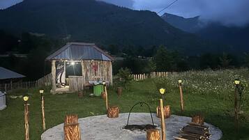 Een rustieke buitenomgeving met een houten constructie en een vuurkuil, omringd door houtblokken.