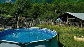 A swimming pool with a mountain backdrop, surrounded by a wooden fence and a small building. - Qvis sakhli (Mestia)