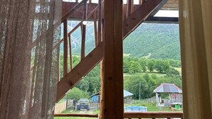 A room with a wooden staircase, a view of a green landscape, and a small outdoor area with a fence. - Qvis sakhli (Mestia)