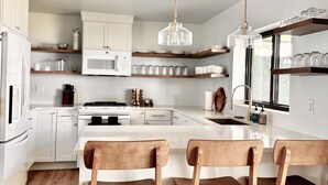 A modern kitchen with white cabinetry, a central island with bar stools, and pendant lighting.