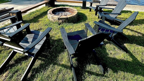 A lakeside deck with Adirondack chairs, a fire pit, and a dock with a boat.
