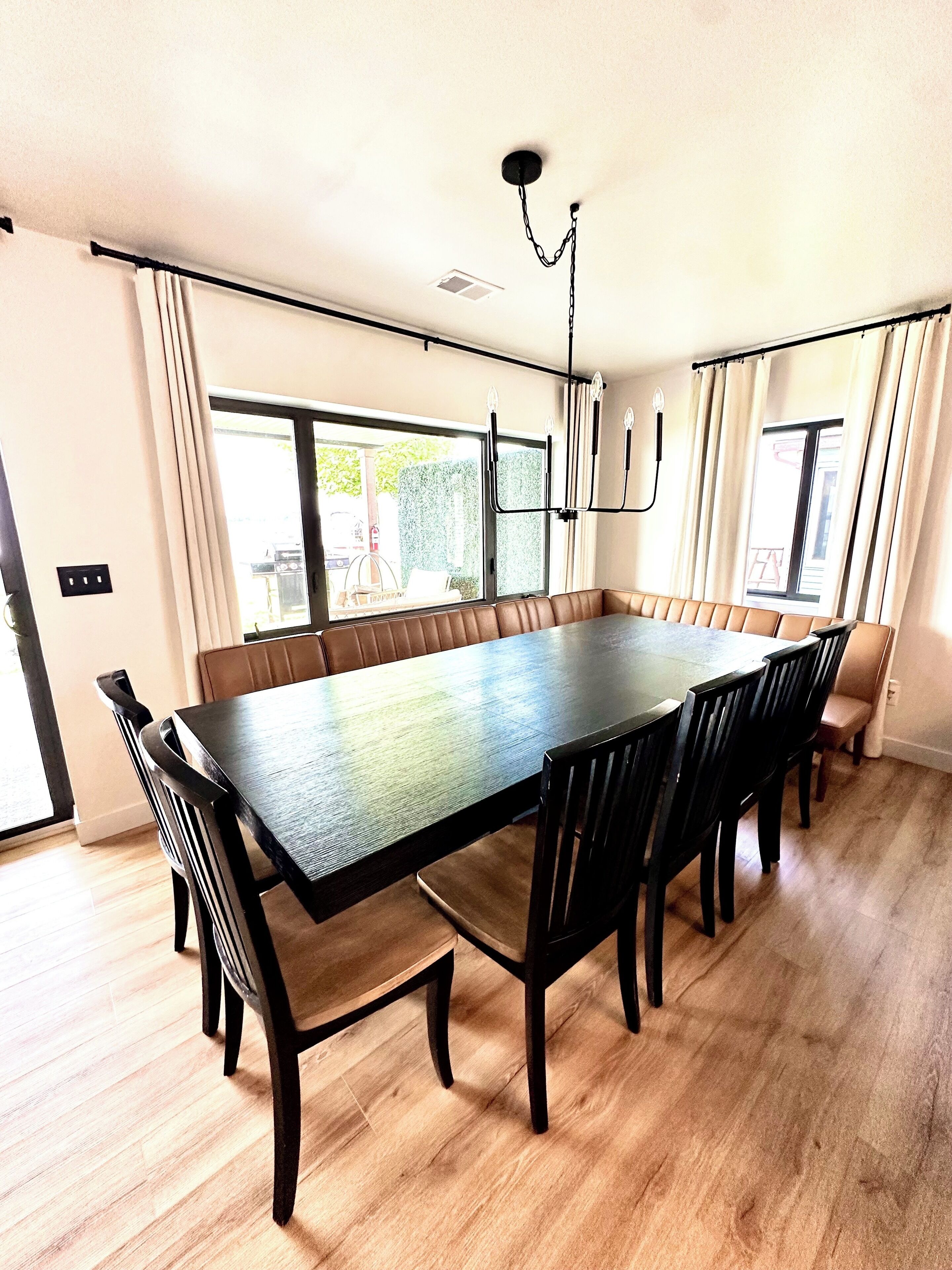 Un comedor amplio con una mesa grande, seis sillas, una araña y ventanas grandes con cortinas.