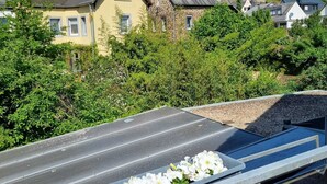 Une vue depuis un balcon doté d’une rambarde en métal, donnant sur une route bordée de maisons et sur un château perché sur une colline.