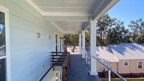 A covered outdoor area with a wooden bench, a railing, and a view of a house in the background. - 2 Connected Apartments · 6BR 4BA · Sleeps 12 · W/D (Moss Point)