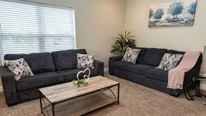 A living room with two dark grey sofas, a wooden coffee table, and a painting on the wall. - 2 Connected Apartments · 6BR 4BA · Sleeps 12 · W/D (Moss Point)