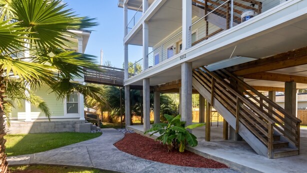A multi-story building with a covered outdoor area, a staircase, and a well-maintained lawn. - 2 Connected Apartments · 6BR 4BA · Sleeps 12 · W/D (Moss Point)