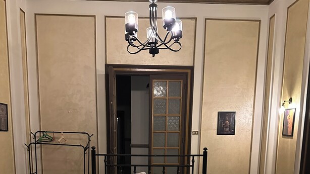 A bed with a metal frame, a chandelier, a wooden door, and a wall-mounted picture frame.