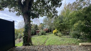 A garden with a wooden deck, a tree, and various plants. - Peaceful Home With Terrace & Parking (Le Mans)