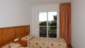 A bedroom with a wooden headboard, a bed with floral bedding, a window with a view, and a striped curtain. - Apartment in Spain Near Sandy Beach (Torroella de Montgrí)