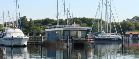 A marina with boats docked, a small building with a glass facade, and a rocky shoreline.