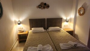 Une chambre double avec deux lits, chacun doté d’une tête de lit et de tables de chevet. Des lampes murales sont fixées de chaque côté des lits, et un élément décoratif orne le mur au-dessus des lits.