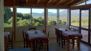 Un espace repas avec des tables et des chaises, de grandes fenêtres offrant une vue sur des collines verdoyantes et des montagnes.