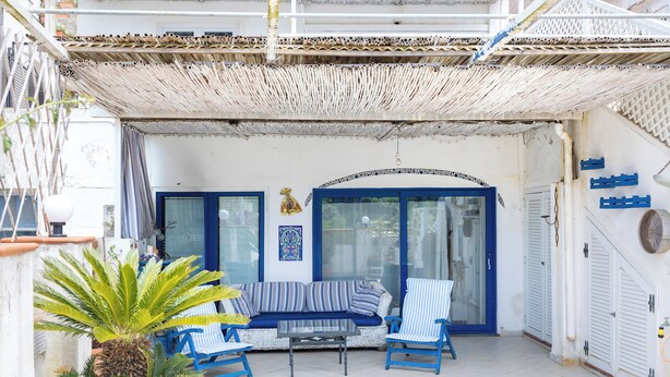 A covered outdoor seating area with a sofa and chairs, a potted plant, and a decorative wall piece.