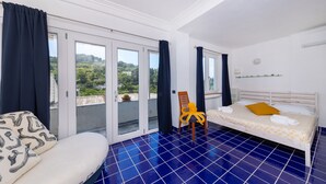 A bedroom with a bed, a chair, a view through a sliding door, and a tiled floor.